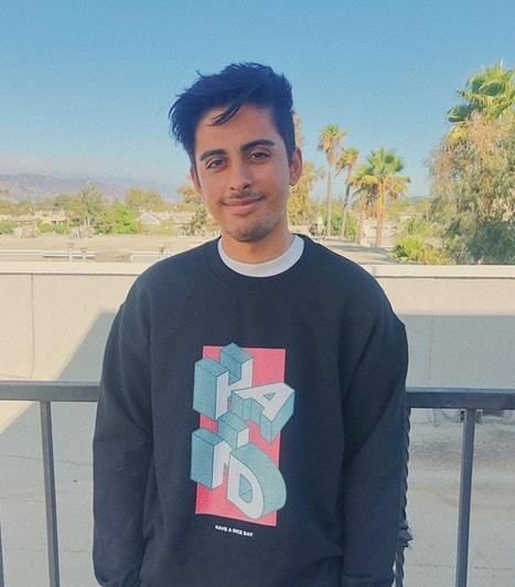 a man standing in front of a metal fence wearing a black sweatshirt with the letter s on it