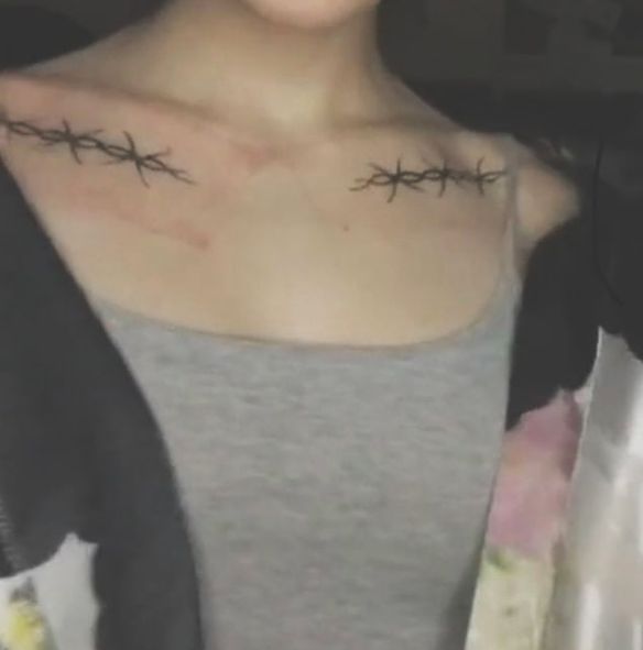 a woman with barbed wire tattoos on her chest and shoulder, looking at the camera