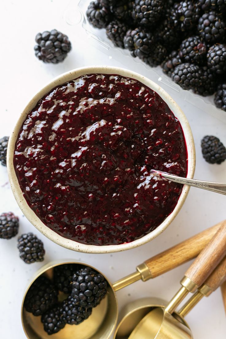 a bowl filled with berries next to two measuring spoons and some blackberries on the table