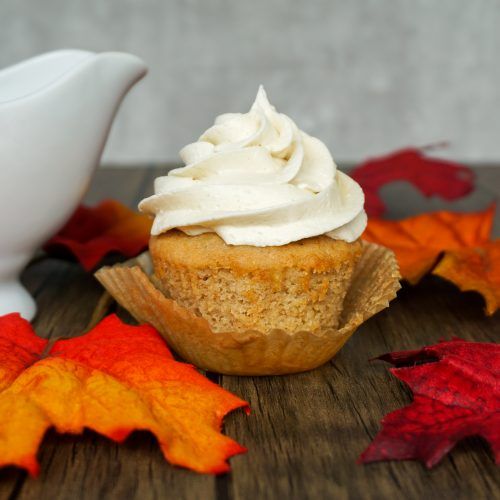 a cupcake sitting on top of a wooden table next to leaves and a white pitcher