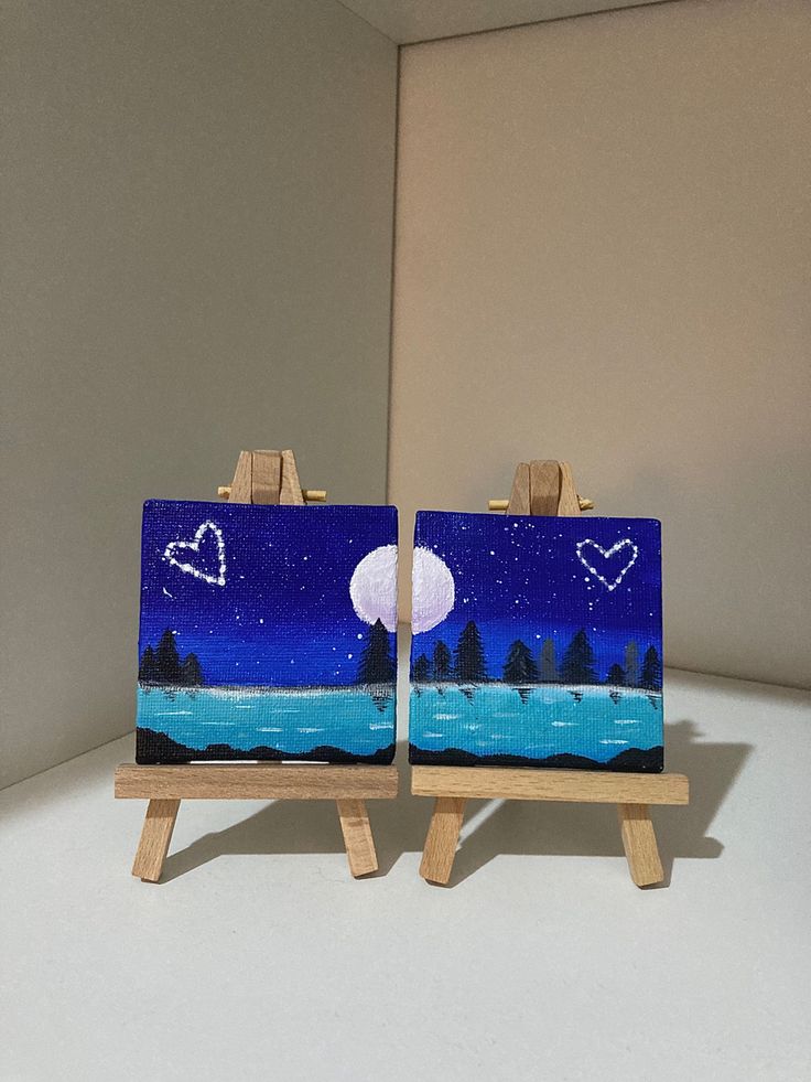 two small easels with paintings on them in the shape of hearts and trees at night