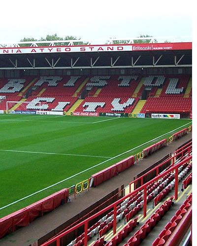 an empty stadium filled with red seats and green grass covered in white letters on the sidelines