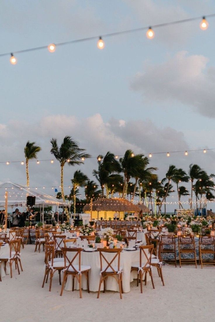 tables and chairs are set up on the beach for an outdoor wedding reception at dusk