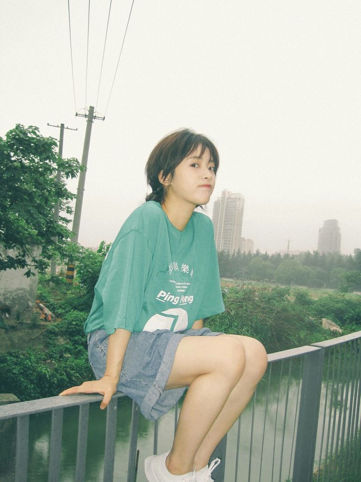 a young woman sitting on top of a metal rail next to a river and power lines