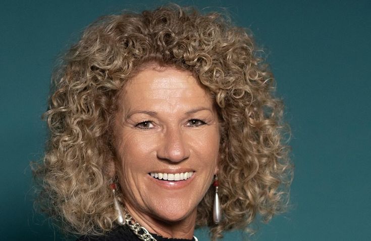 a woman with curly hair smiling at the camera and wearing large earrings on her head