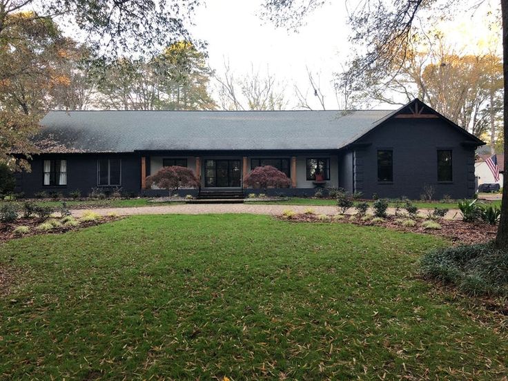 a large black house in the middle of a yard with trees and bushes around it