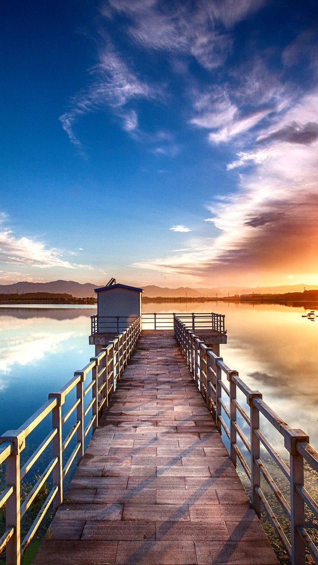 a wooden pier sitting on top of a lake under a cloudy blue sky at sunset