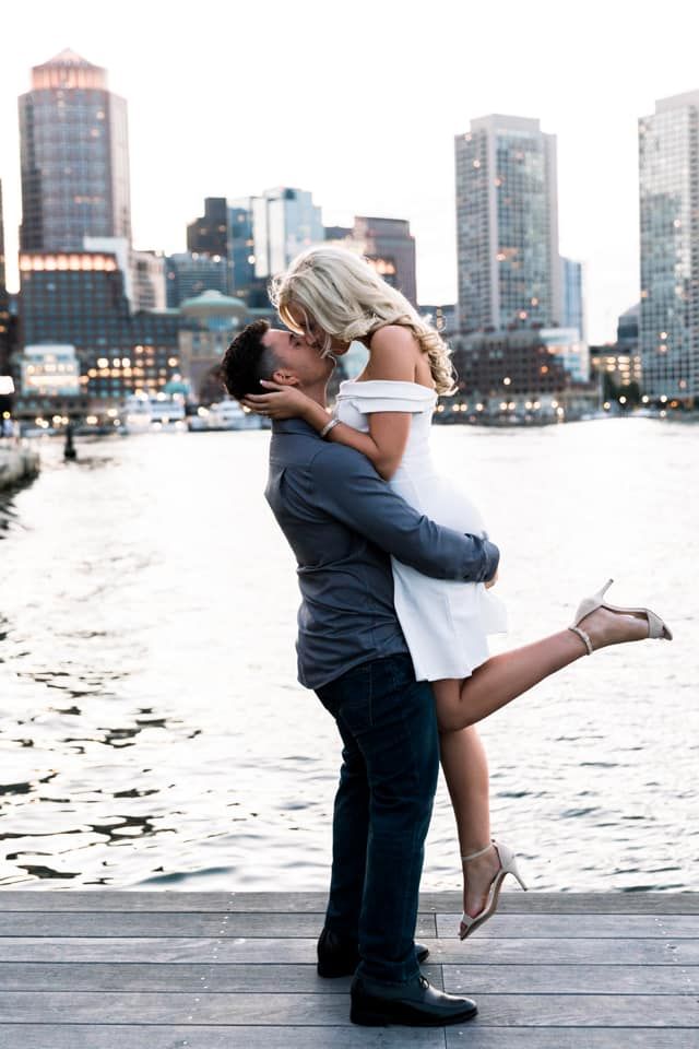 a man and woman kissing in front of a body of water with buildings in the background