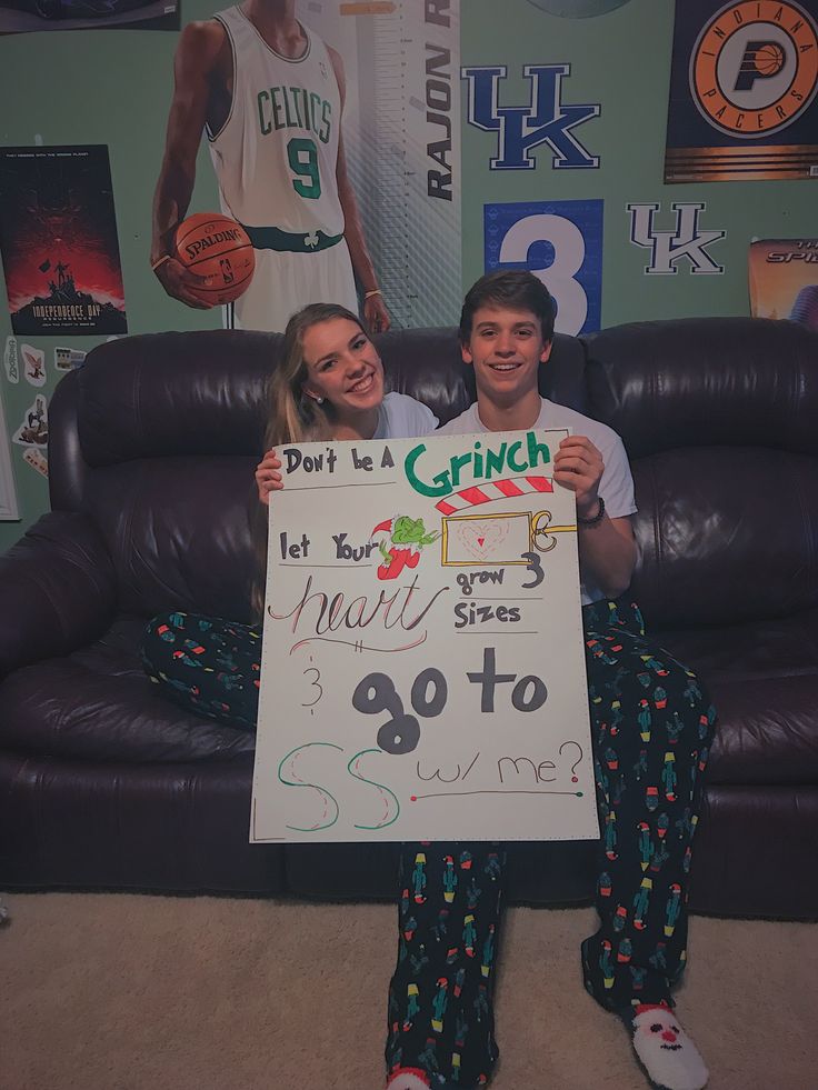 two people sitting on a couch holding up a sign