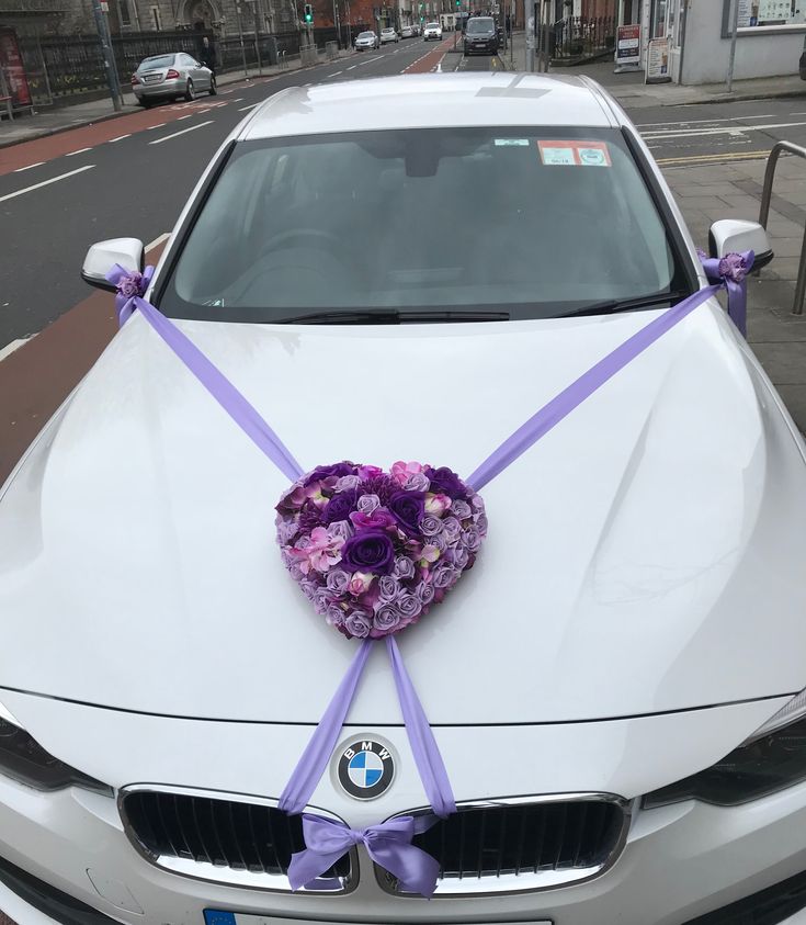 a white car with purple flowers tied to the hood