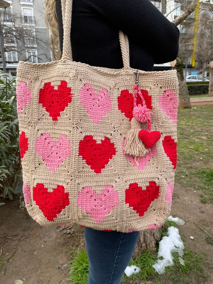 a woman carrying a crocheted bag with hearts on it