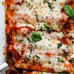 a casserole dish with meat, cheese and spinach leaves on the side