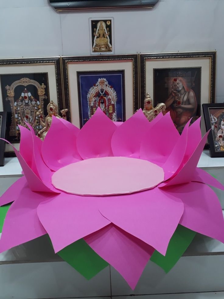 a pink paper lotus flower sitting on top of a table next to pictures and frames