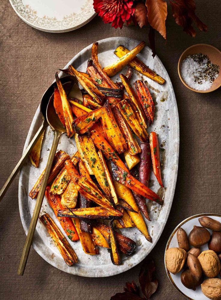 roasted carrots and potatoes on a white plate with gold spoons next to them