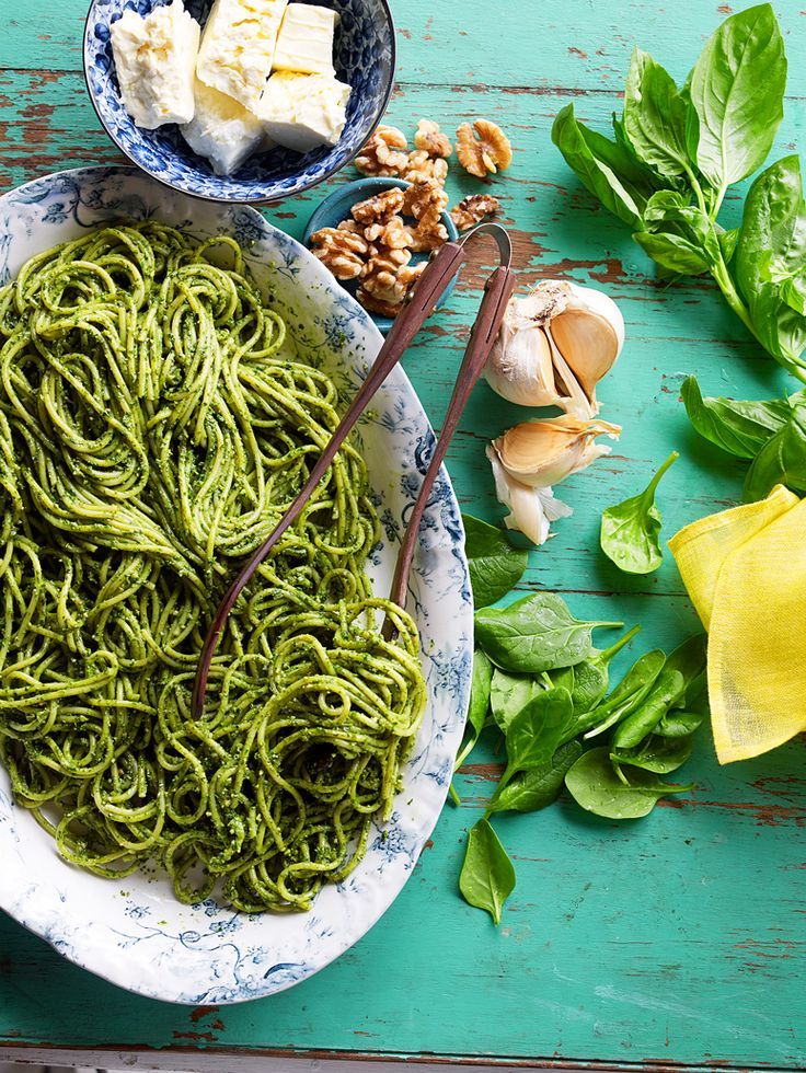 green pasta with pesto sauce, walnuts and spinach on a blue wooden table