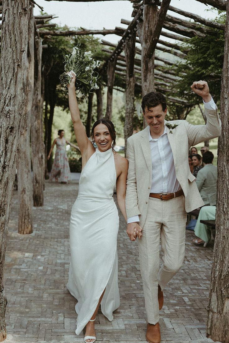 a man and woman walking down a path holding hands in the air with trees behind them