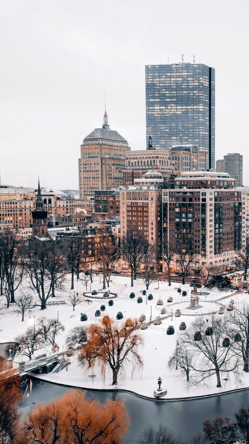 the city skyline is covered in snow and surrounded by tall buildings, trees, and benches