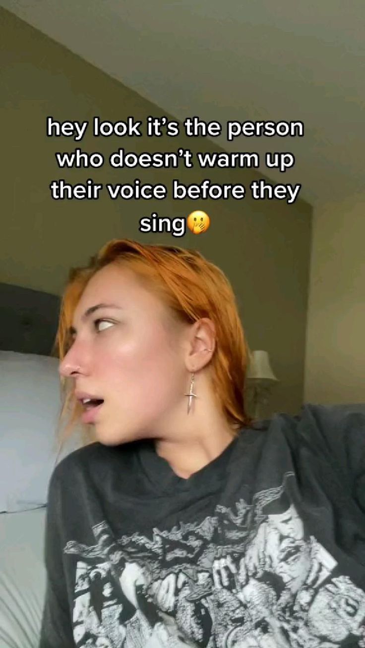 a woman with red hair is talking on her cell phone while wearing a t - shirt that says, they look it's the person who doesn't warm up their voice before they sing