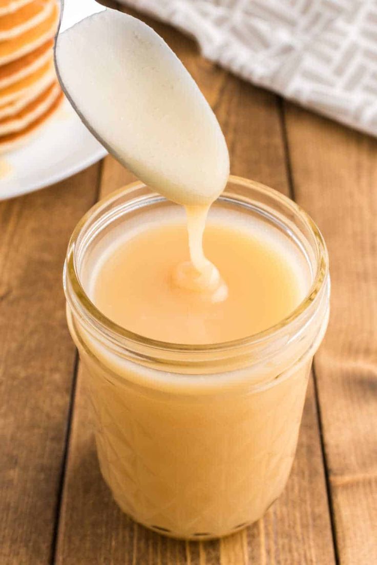 a spoon full of peanut butter sitting on top of a wooden table next to some pancakes