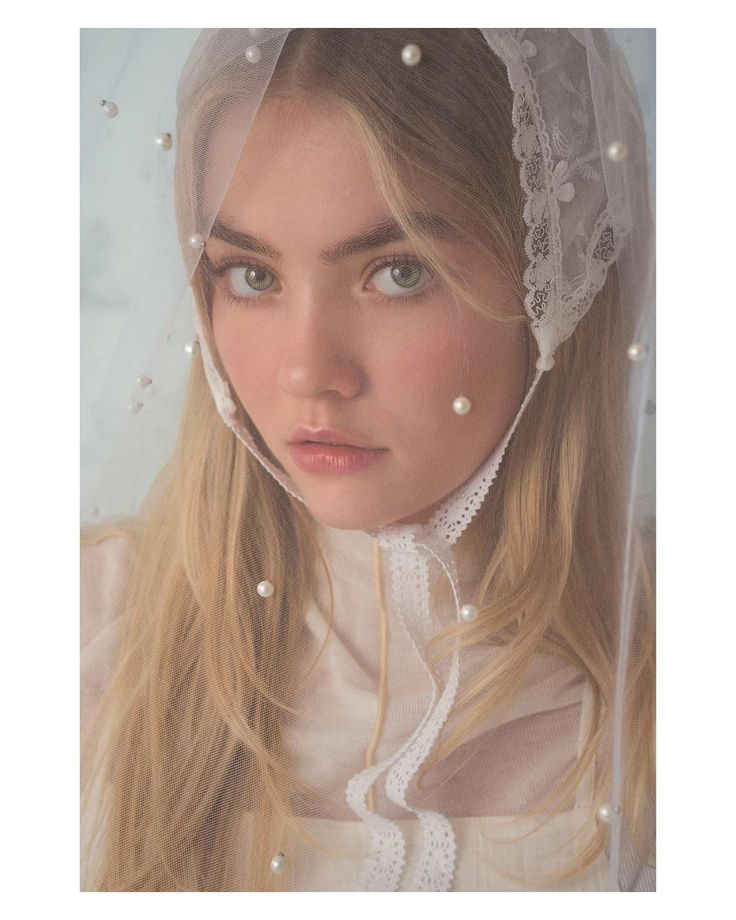 a woman with long blonde hair wearing a veil over her head and pearls around her neck