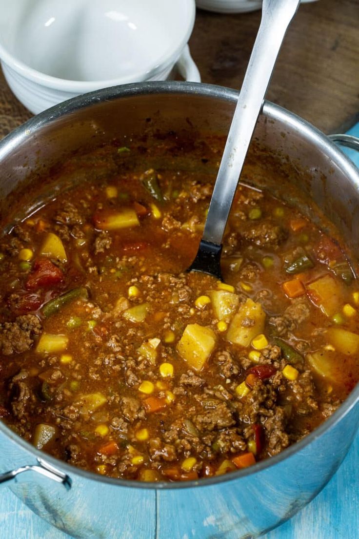 a large pot filled with soup on top of a blue table next to white dishes