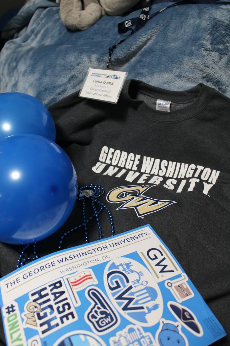 some blue balloons and a black t - shirt on a bed with a stuffed animal