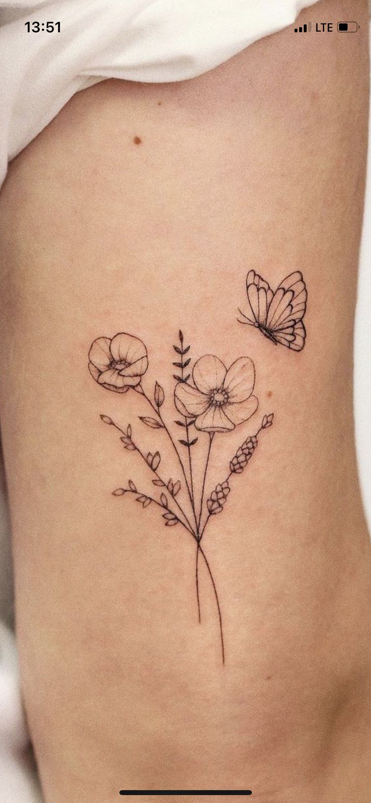 a small flower tattoo on the side of a woman's stomach, with two butterflies flying over it