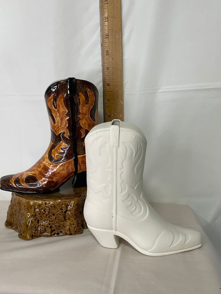 two white cowboy boots sitting on top of a wooden stump next to a ruler and measuring tape