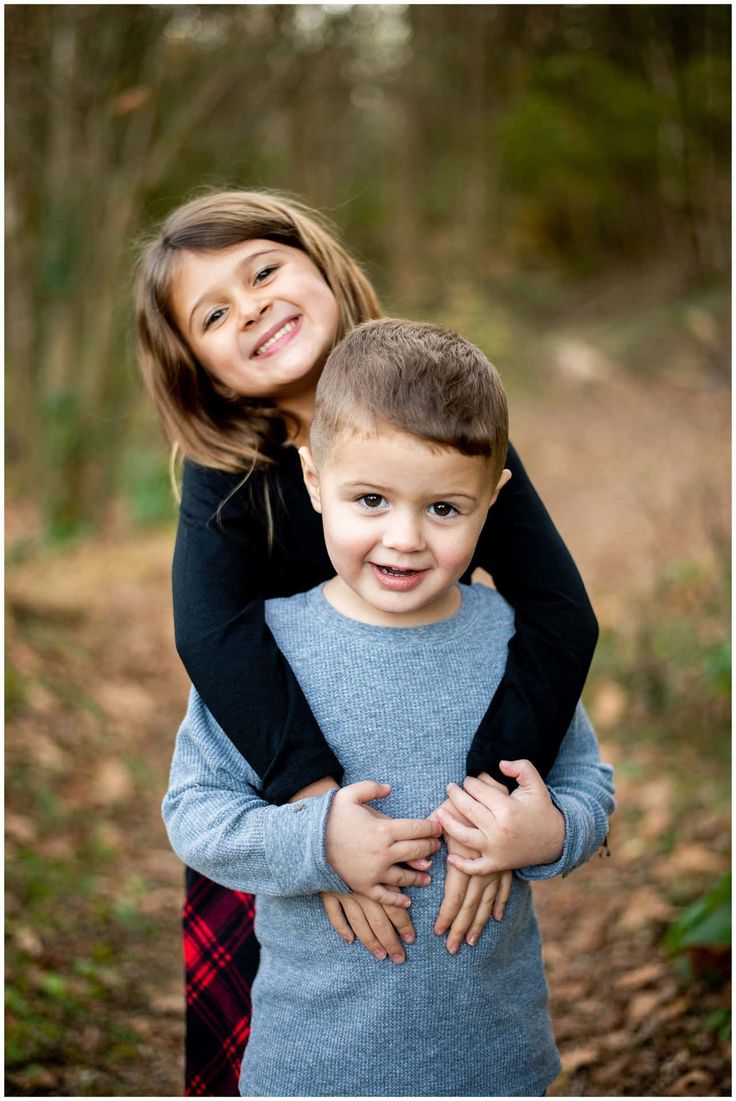 two young children hugging each other in the woods at their family's portrait session