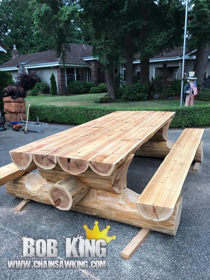 a table made out of logs sitting in the middle of a parking lot next to a house