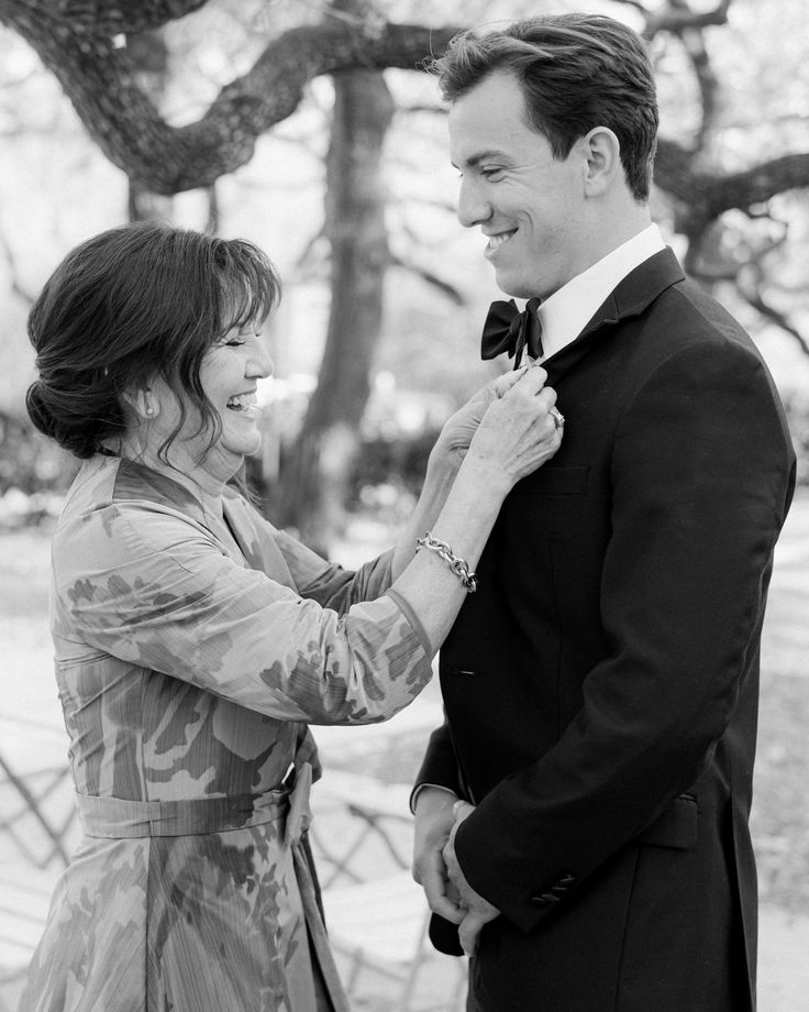 a man adjusting the tie of a woman's dress while standing next to a tree