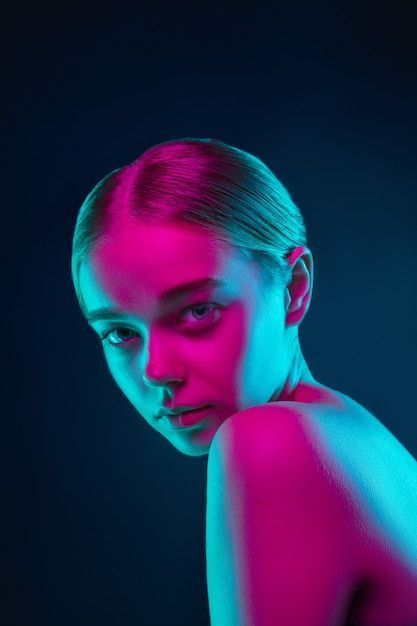 a woman with pink and blue light on her body is looking at the camera while standing in front of a black background