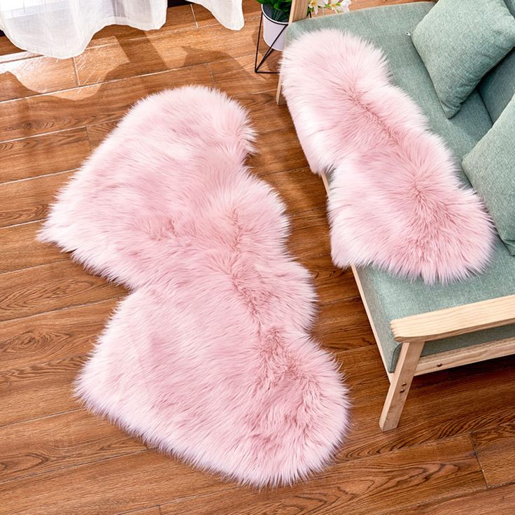 two pink furry rugs sitting on top of a wooden floor next to a couch