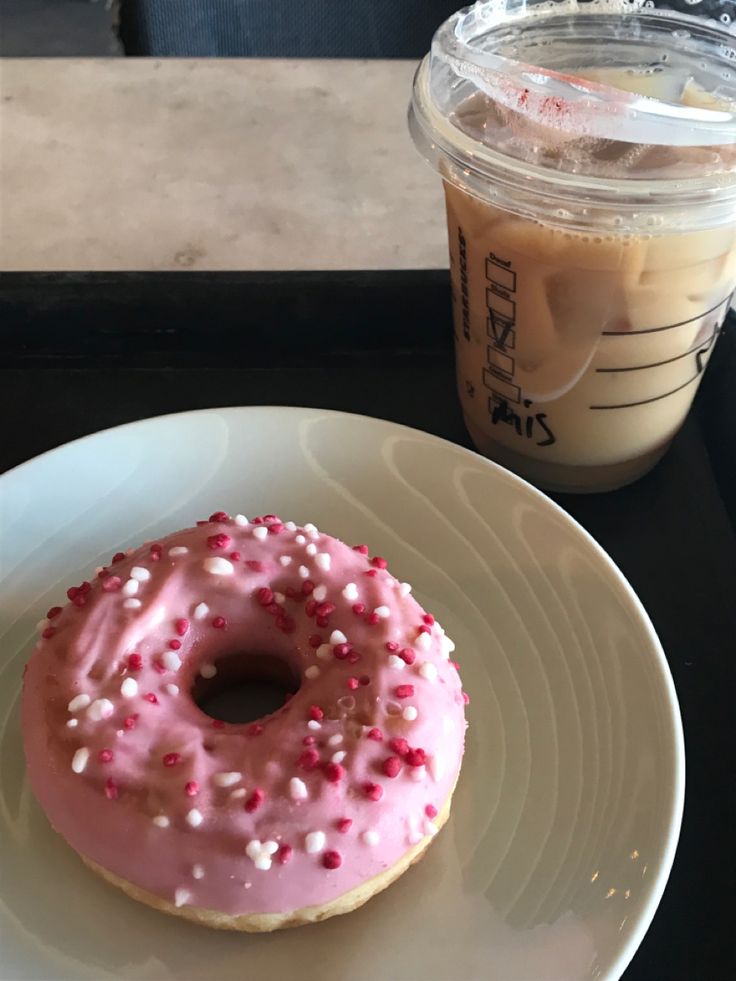 a donut with pink icing and sprinkles on a plate next to a cup of coffee