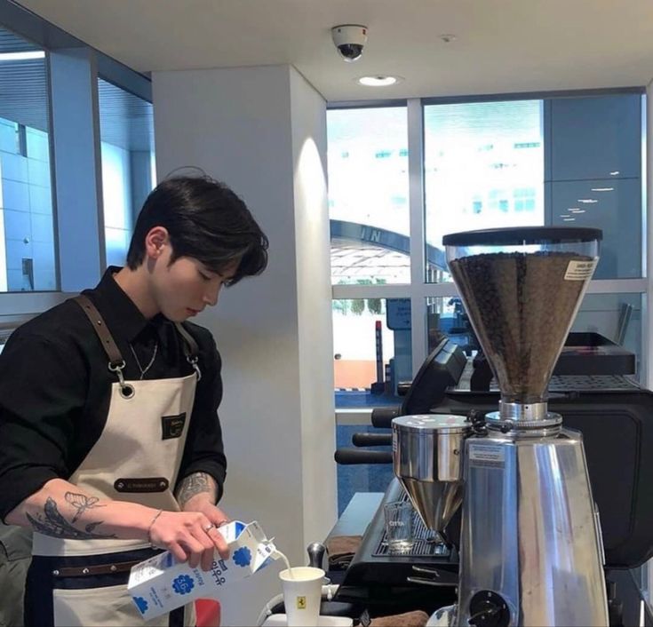 a man standing in front of a coffee maker pouring something into a cup on top of a counter