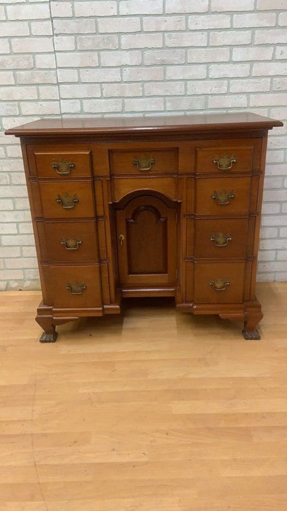 an old wooden desk with two drawers and one door on the top, in front of a brick wall