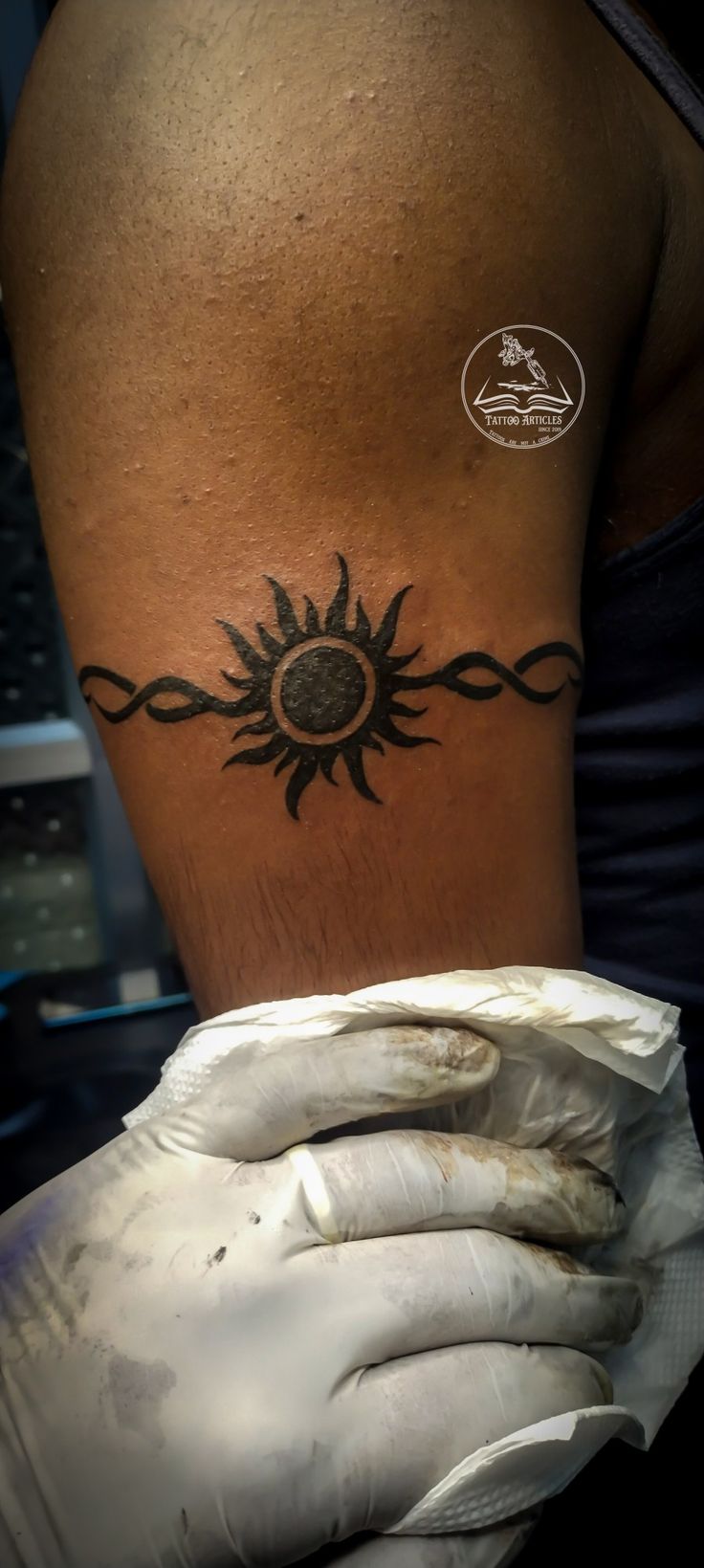 a woman's arm with a sun tattoo on her left shoulder and white gloves