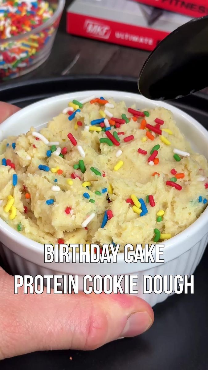 a hand holding a bowl filled with birthday cake protein cookie dough and sprinkles