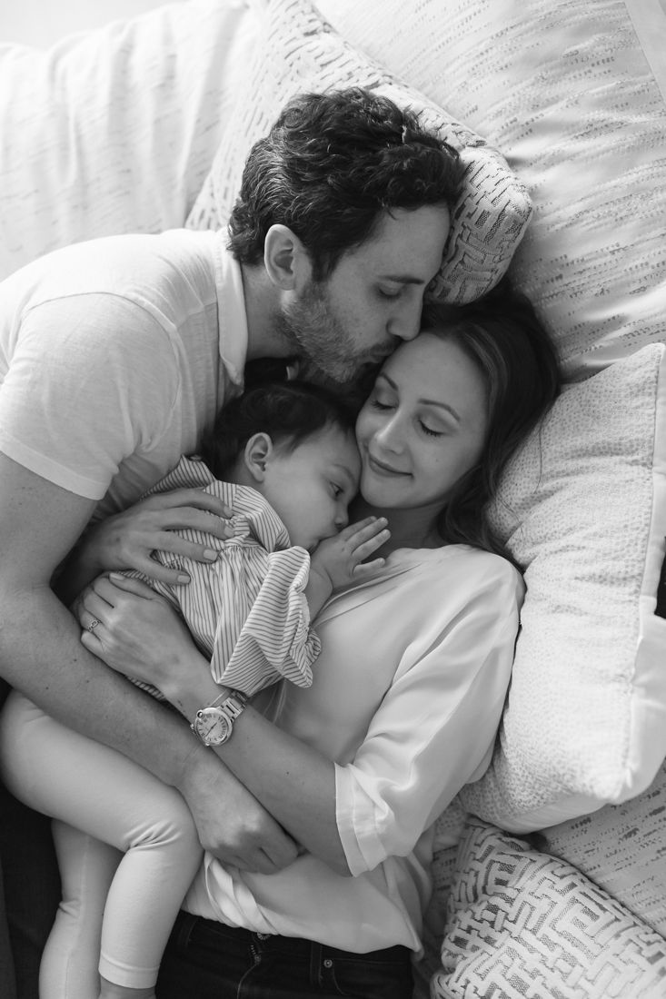 a man and woman are cuddling with a baby on a bed in black and white