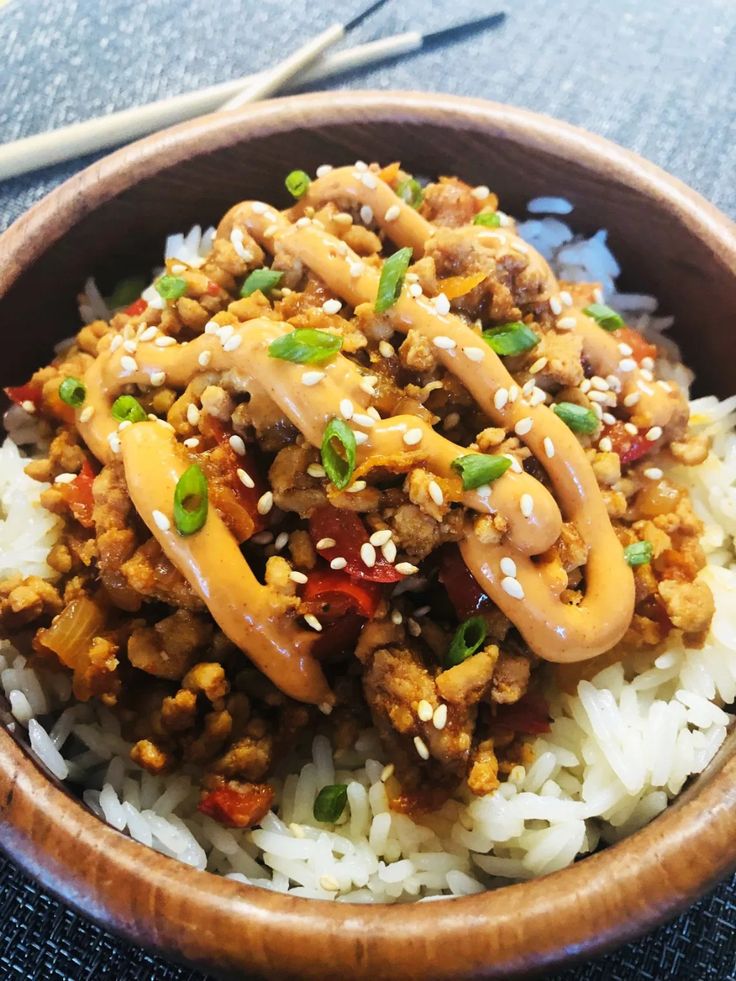 a wooden bowl filled with rice and meat covered in sauce on top of blue table cloth