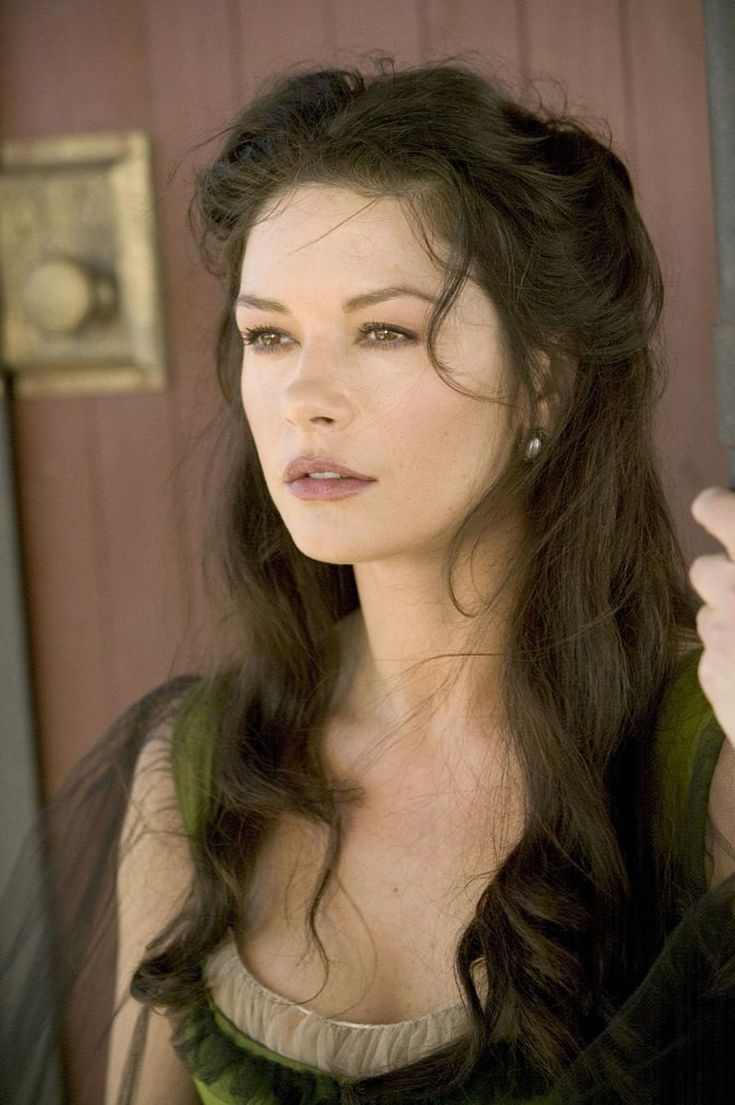 a woman with long dark hair wearing a green dress and holding her hand up to her ear