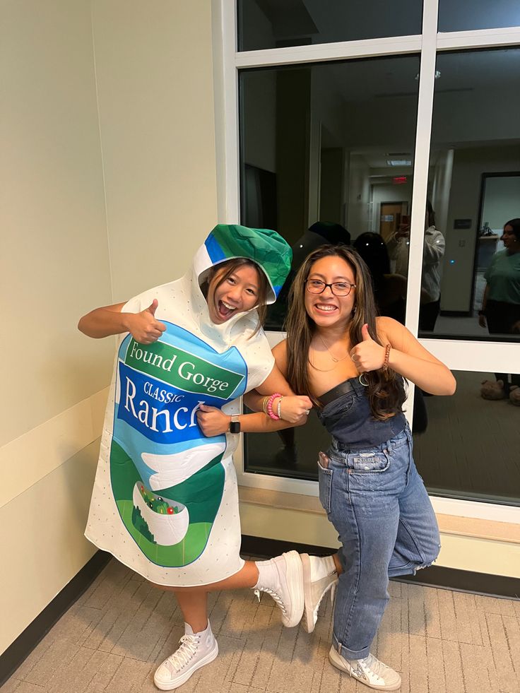 two women in costumes posing for the camera with their arms around each other while one woman holds up a sign