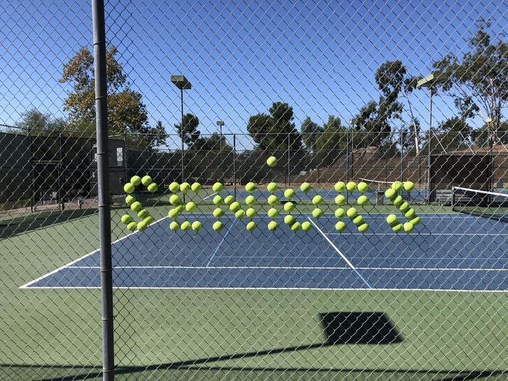 several tennis balls are falling off the racket in front of a fence on a tennis court