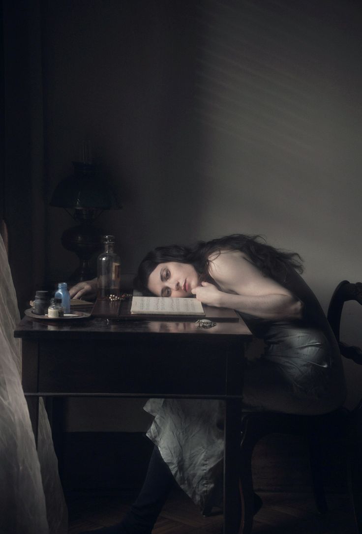 a woman is laying down on the table with her head resting on a book, next to a window