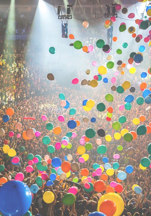 many balloons are floating in the air above a crowd at a music festival or concert