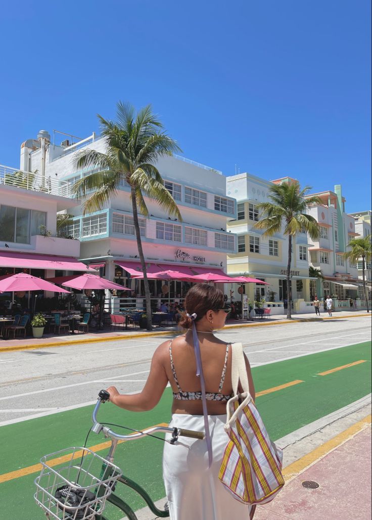 a woman walking down the street with a bike in front of buildings and palm trees