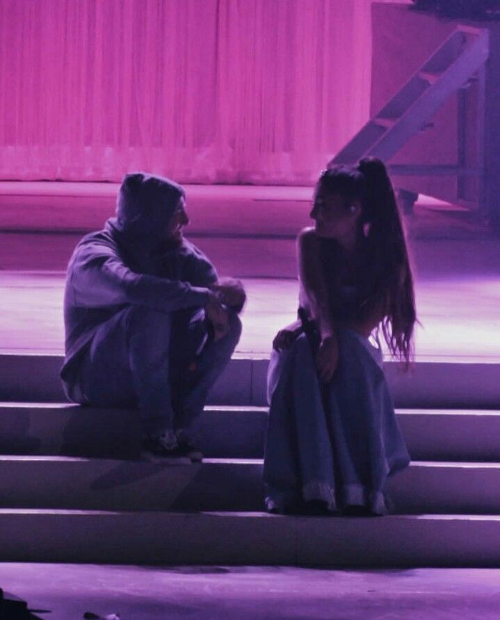 a man and woman sitting on the steps in front of a stage with purple lighting