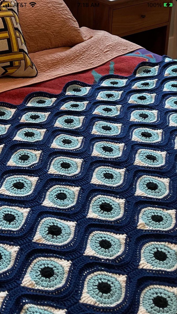 a blue crocheted blanket on top of a bed next to a brown pillow