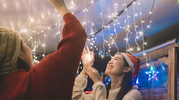 two people are reaching up to the ceiling with christmas lights hanging from it's ceiling