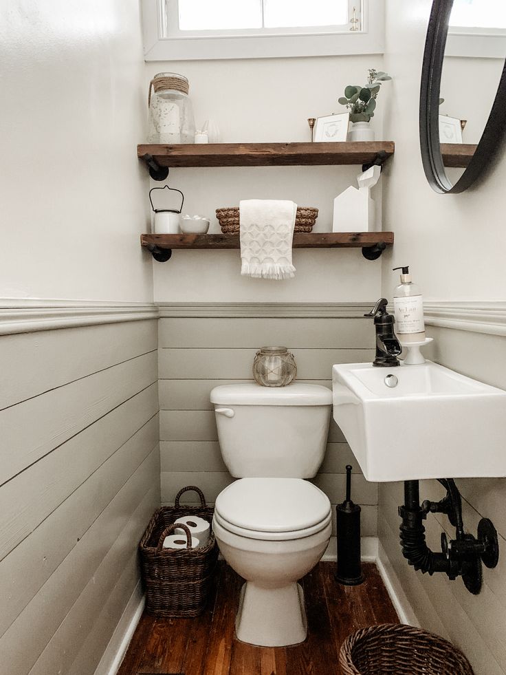 a white toilet sitting in a bathroom next to a sink under a mirror and wooden shelves